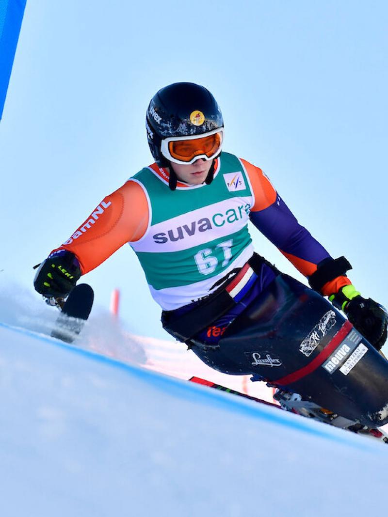 A sit skier going around the gates and skiing down the hill.