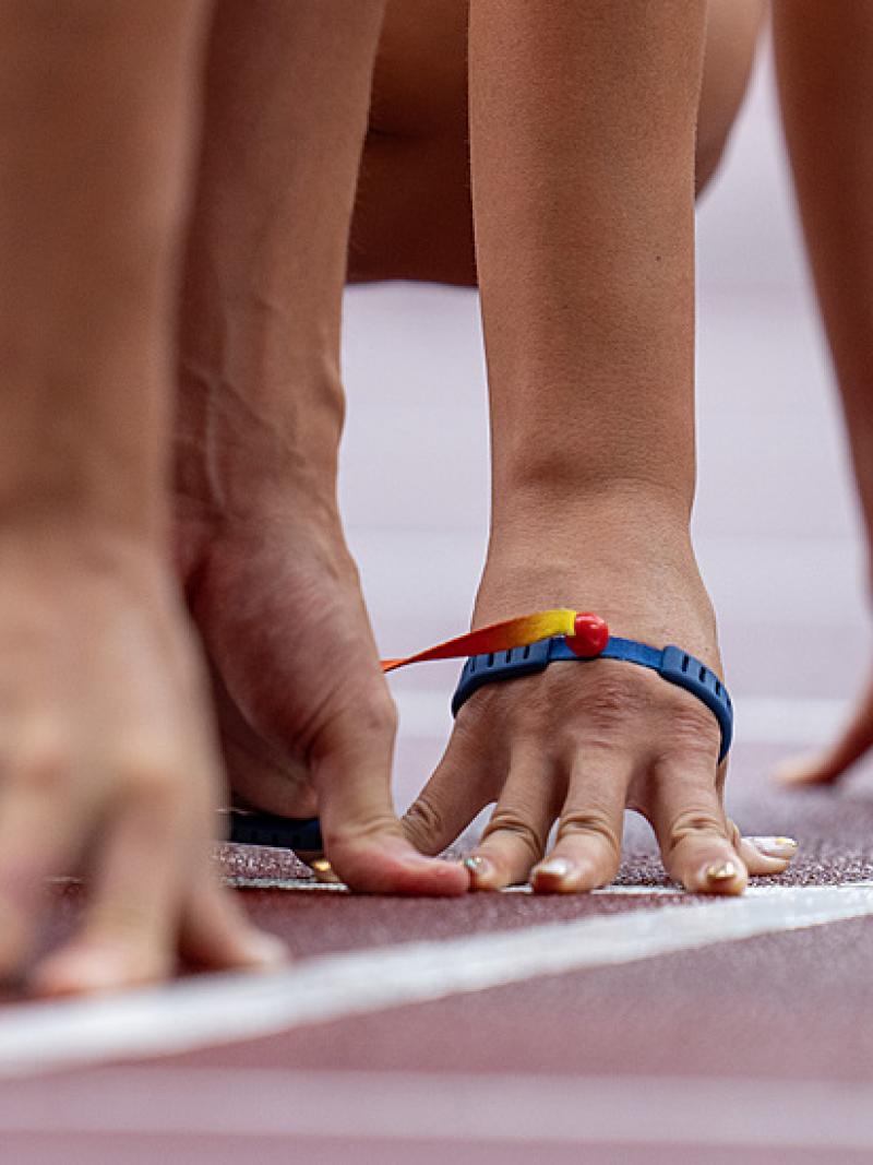 Two pairs of hands side by side on an athletics track starting line