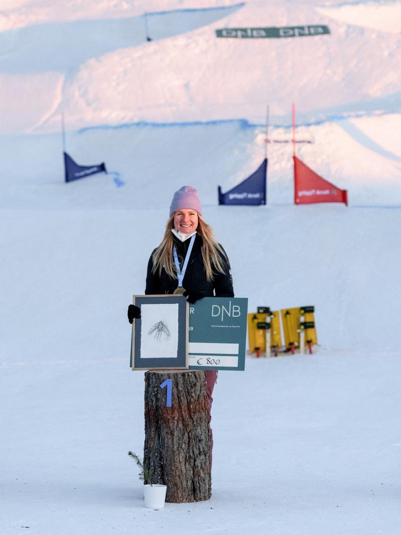 Three women smiling and showing checks in a snowboard medal ceremony in the snow