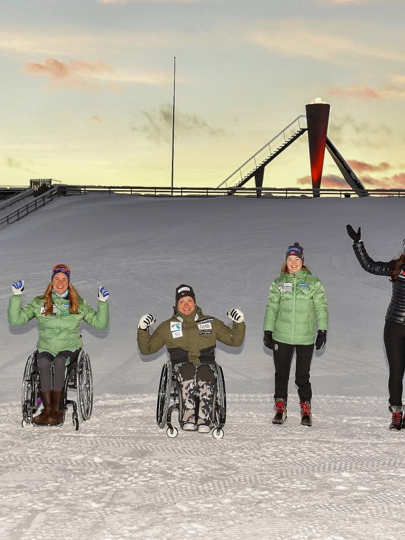 A group of three persons in wheelchairs and four standing persons on the snow