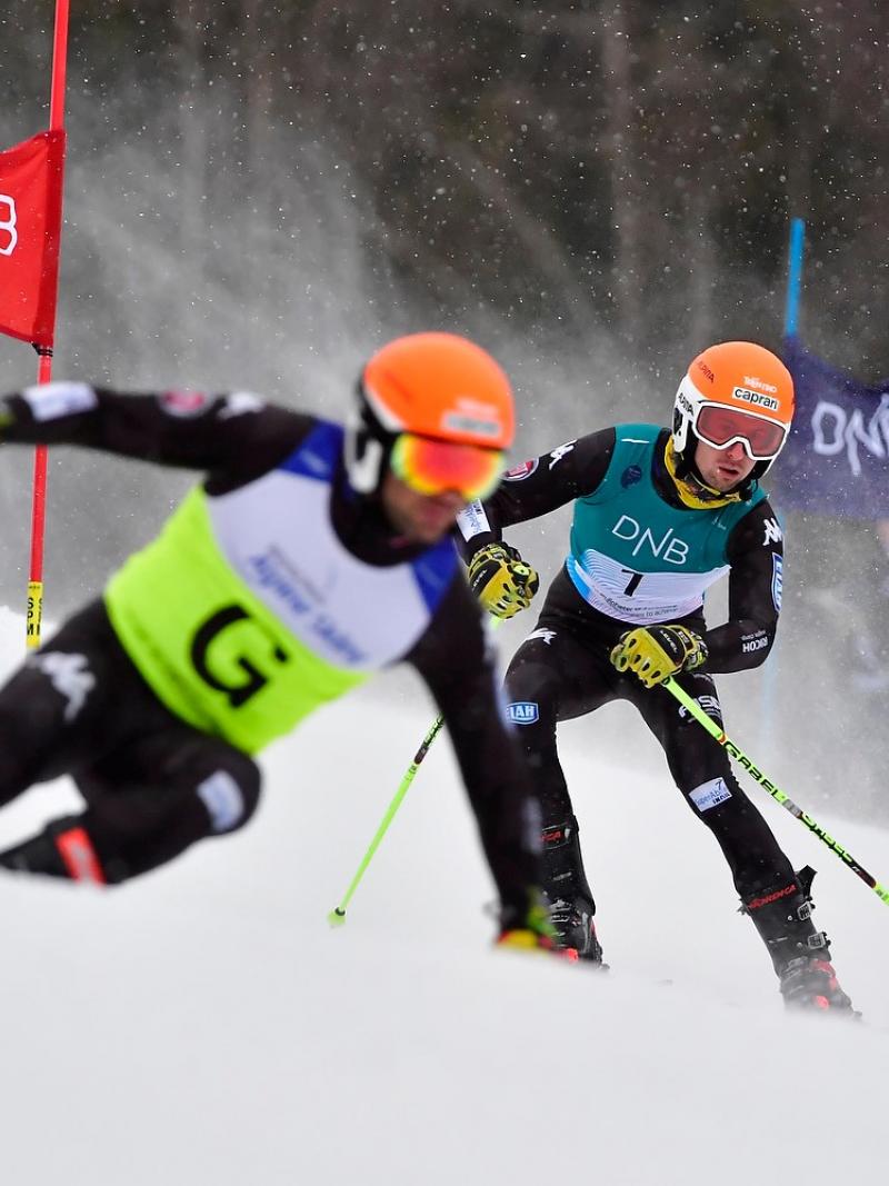 A male Para alpine skier skiing behind his guide in a slalom event