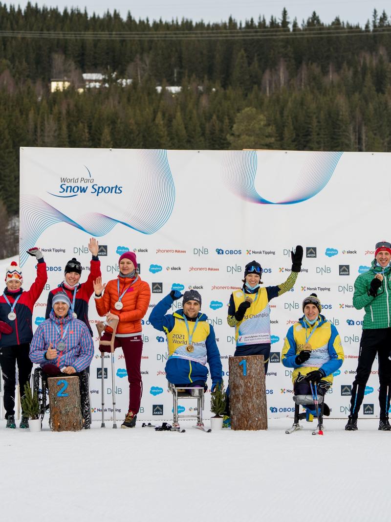 A group of 10 standing persons and four persons in wheelchairs in a medal ceremony on the snow