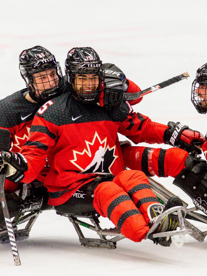 Three players in red and black jerseys smiling and hugging each other on the ice.