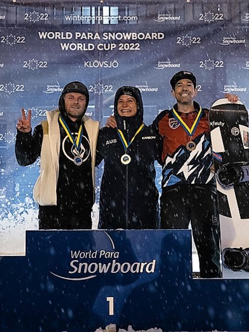 Three men with arms around each other on a snowboard podium