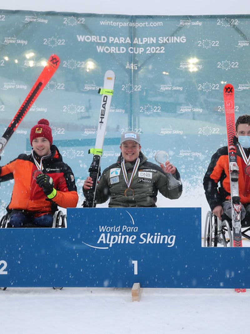 Three men in wheelchairs holding skis in a medal ceremony in the snow