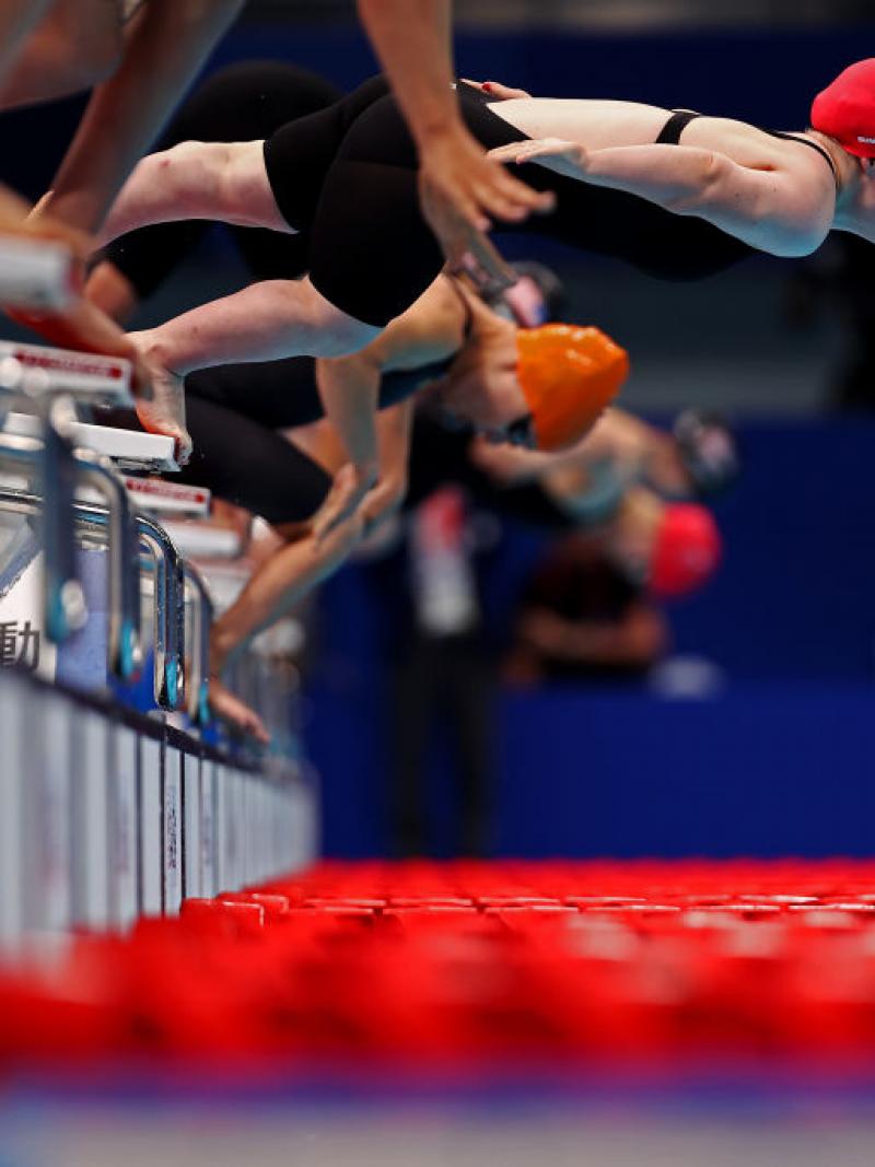 A female swimmers jumping from the starting block ahead of other competitors