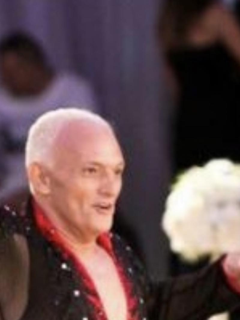 A man wearing a dance costume with his right hand in the air.