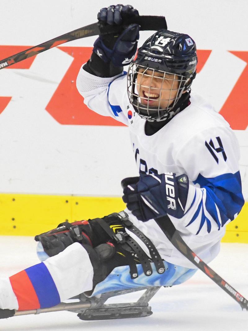 A Para ice hockey player on a sledge celebrates with his right arm raised.