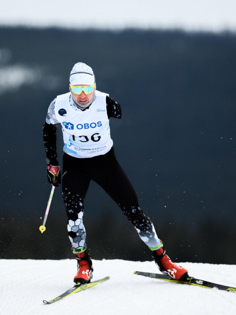 A man with two ski's and one stick in his right hand goes downhill on the snow circuit