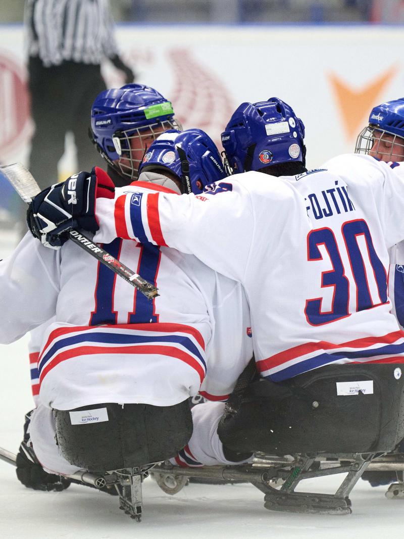 A group of Para ice hockey players on sledges celebrating the victory with a group hug.