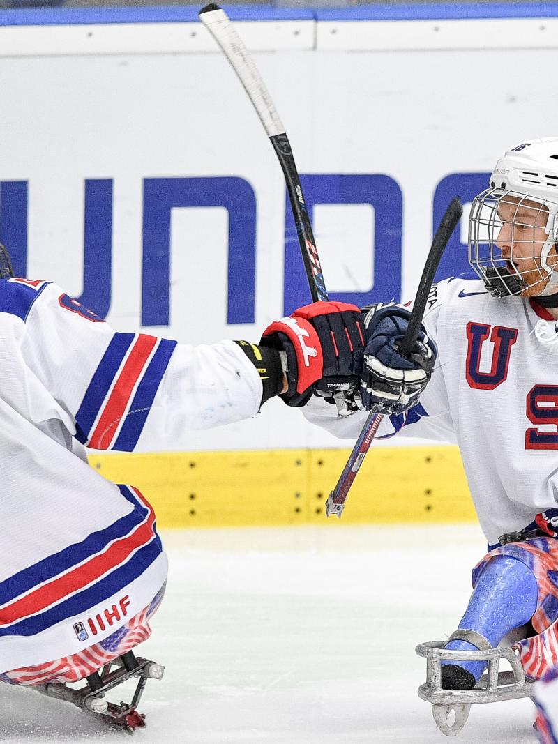 Two Para ice hockey players celebrating with a fist bump on their sledges.
