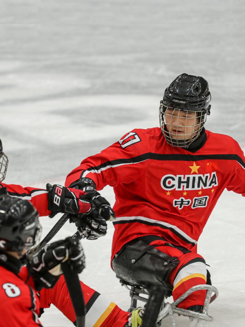 Three Para ice hockey players in red jerseys celebrating with fist bumps.