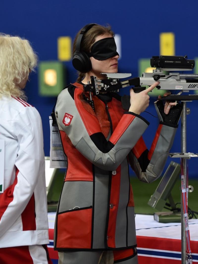 A vision impaired shooter blindfolded with her assistant behind her in a rifle competition