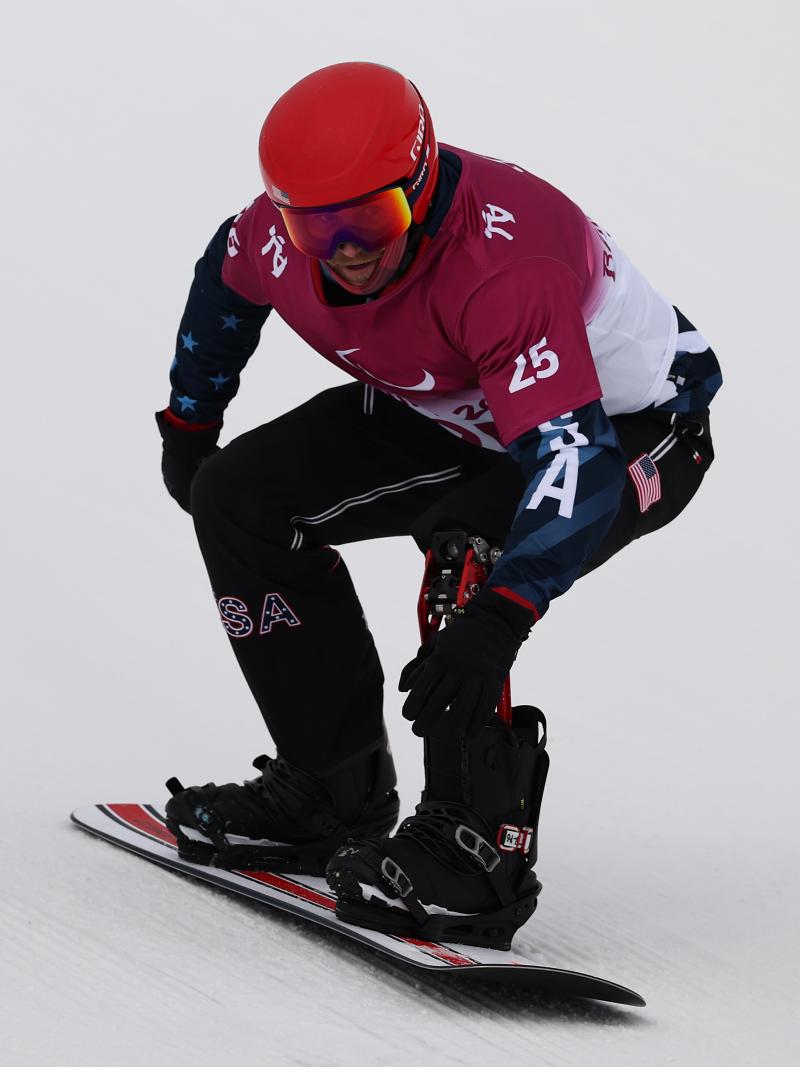 A man on a snowboard going down the snow with a helmet and goggles on his head.
