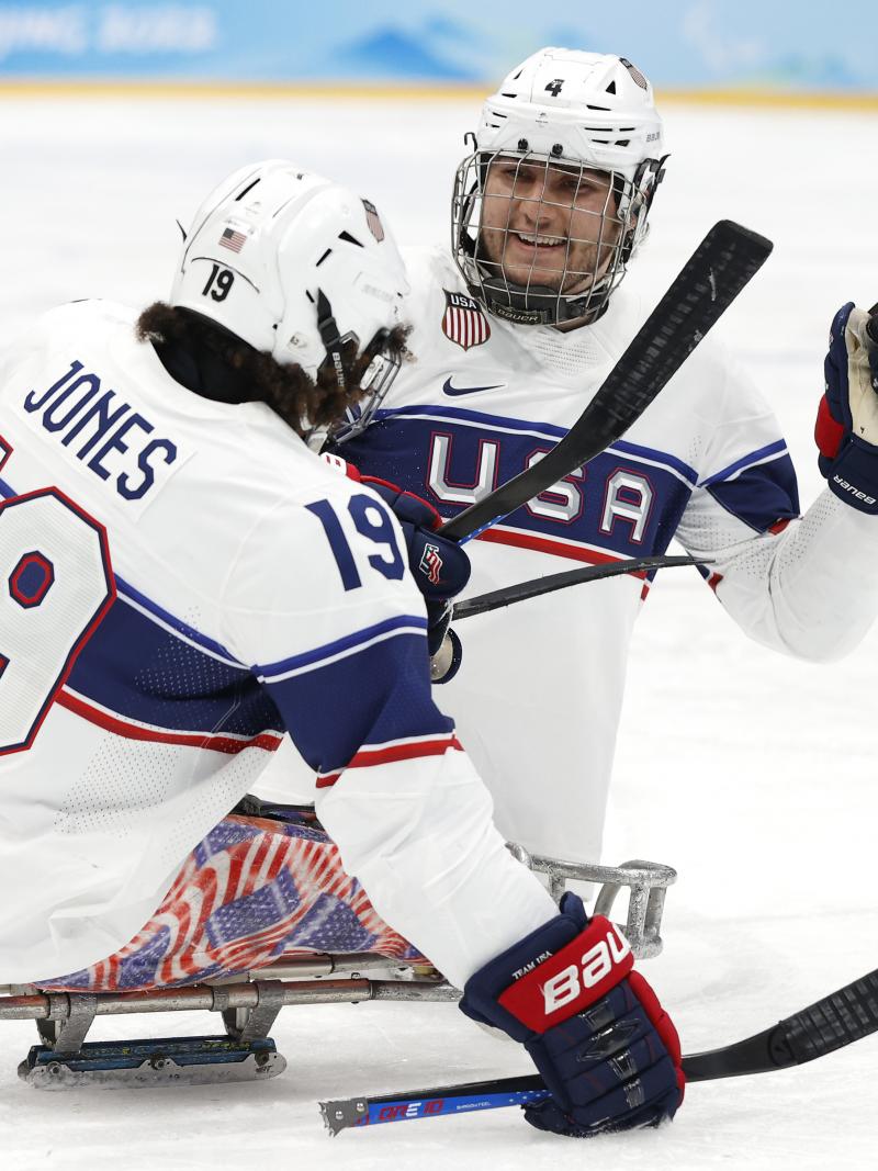 Two Para ice hockey players smiling to each other while on mono sleds.