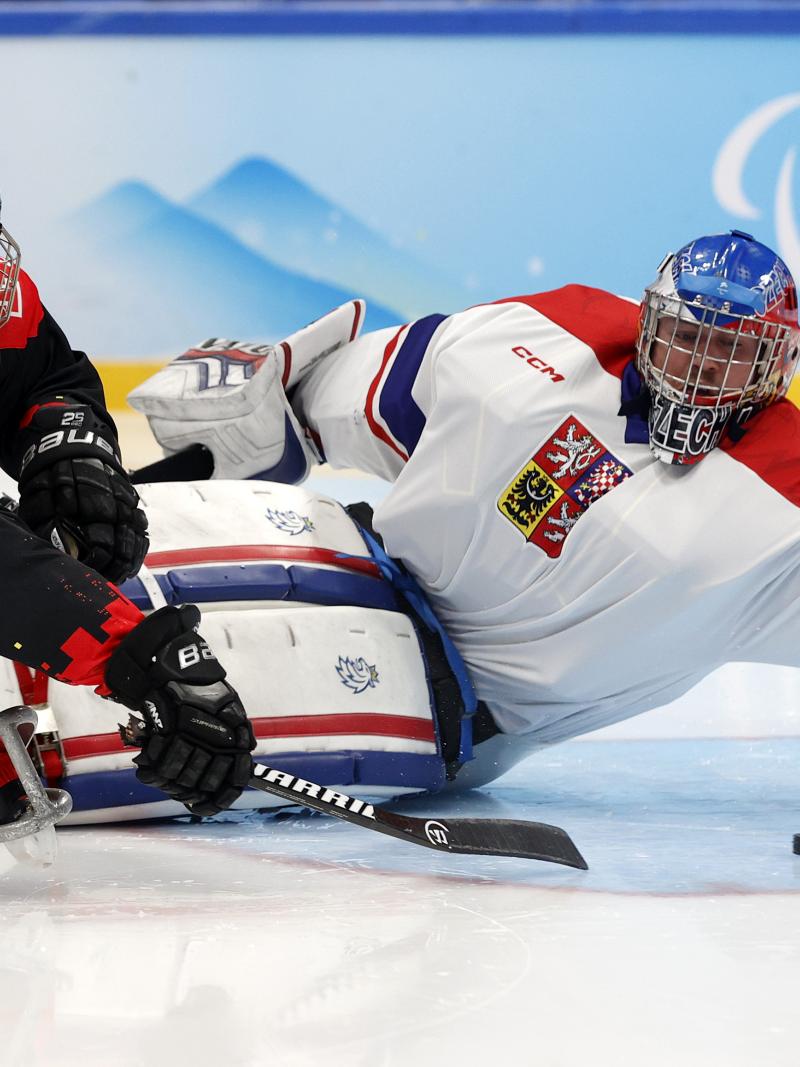 A Para ice hockey player in full gear kicks the puck with a stick past the goalie who throws himself on the ice.