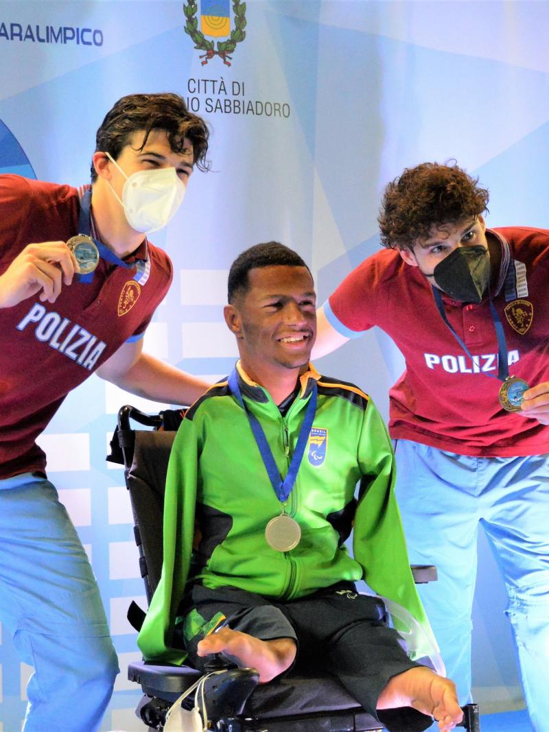 A man in a wheelchair in a medal ceremony with two standing men by his side