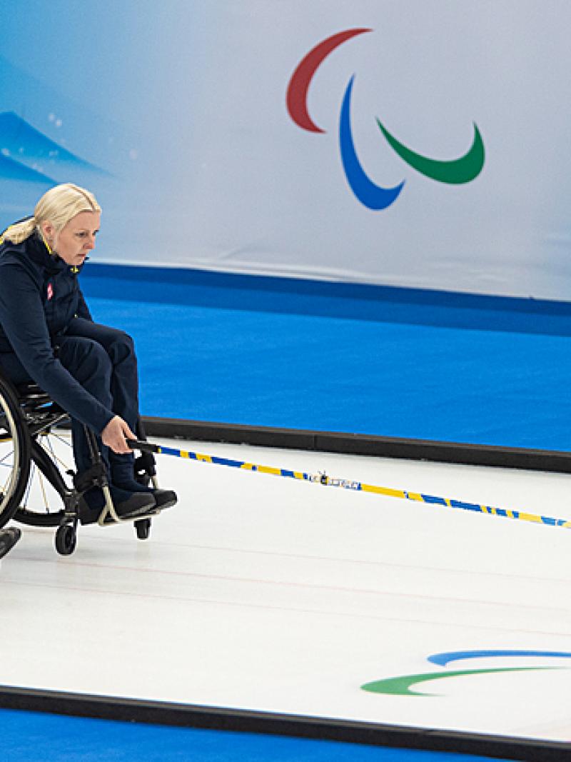 A Swedish wheelchair curler pushes the stone forward while her teammates looks on
