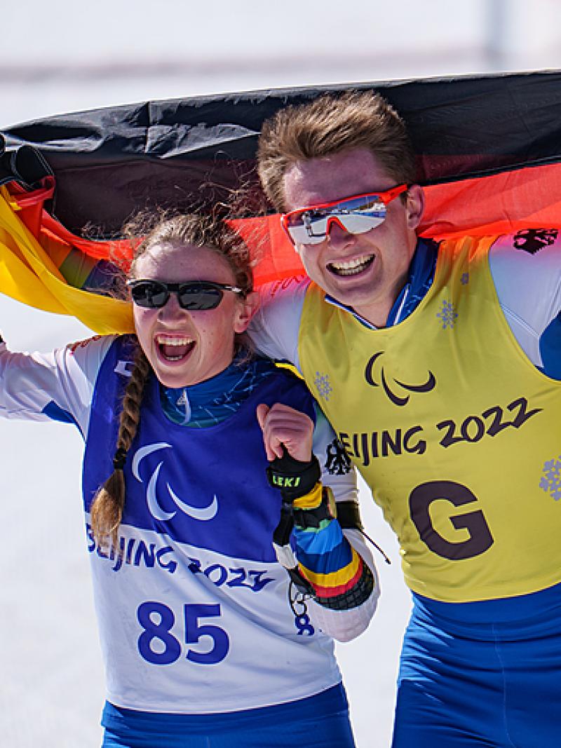 Leonie Maria Walter and Guide Pirmin Strecker hold the German flag behind them as they celebrate winning