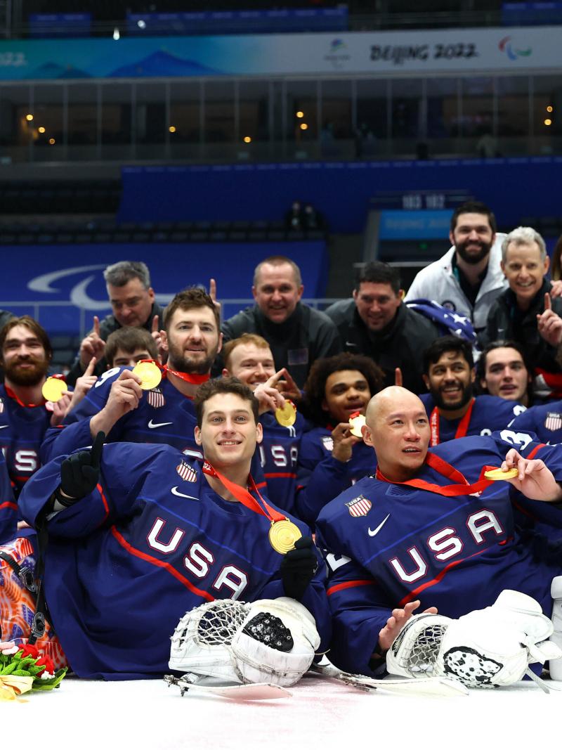 Team USA Para ice hockey players in full gear without helmets posing for a photo with gold medals.