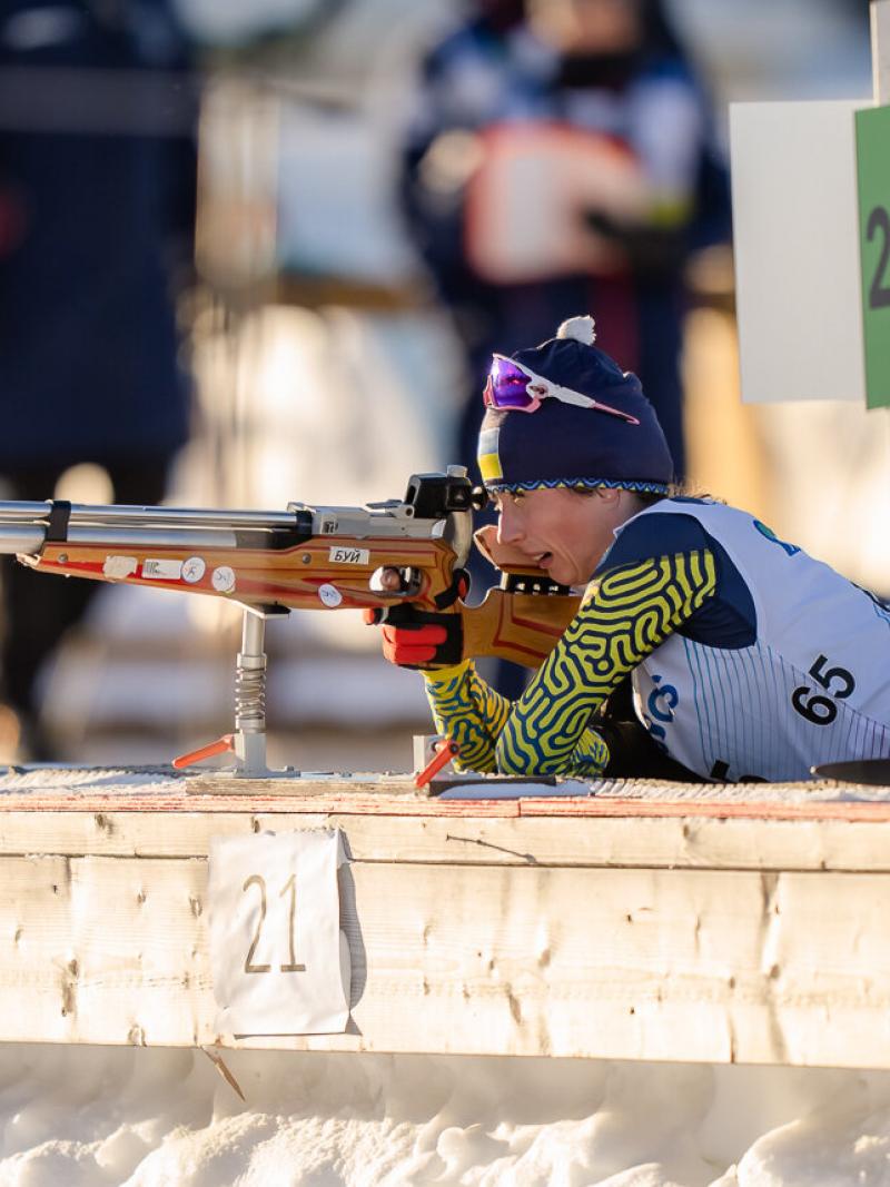 A female athlete lying on the floor aiming with the rival in her hands.