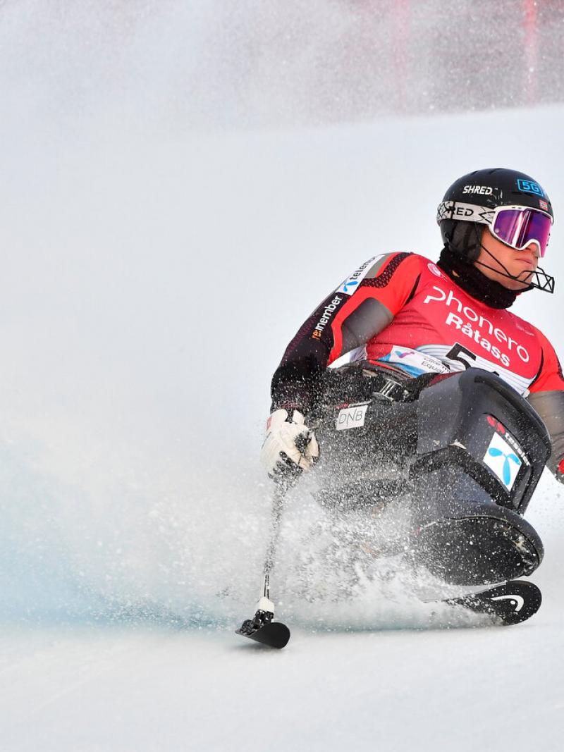 A man in a sit ski sliding into the snow.