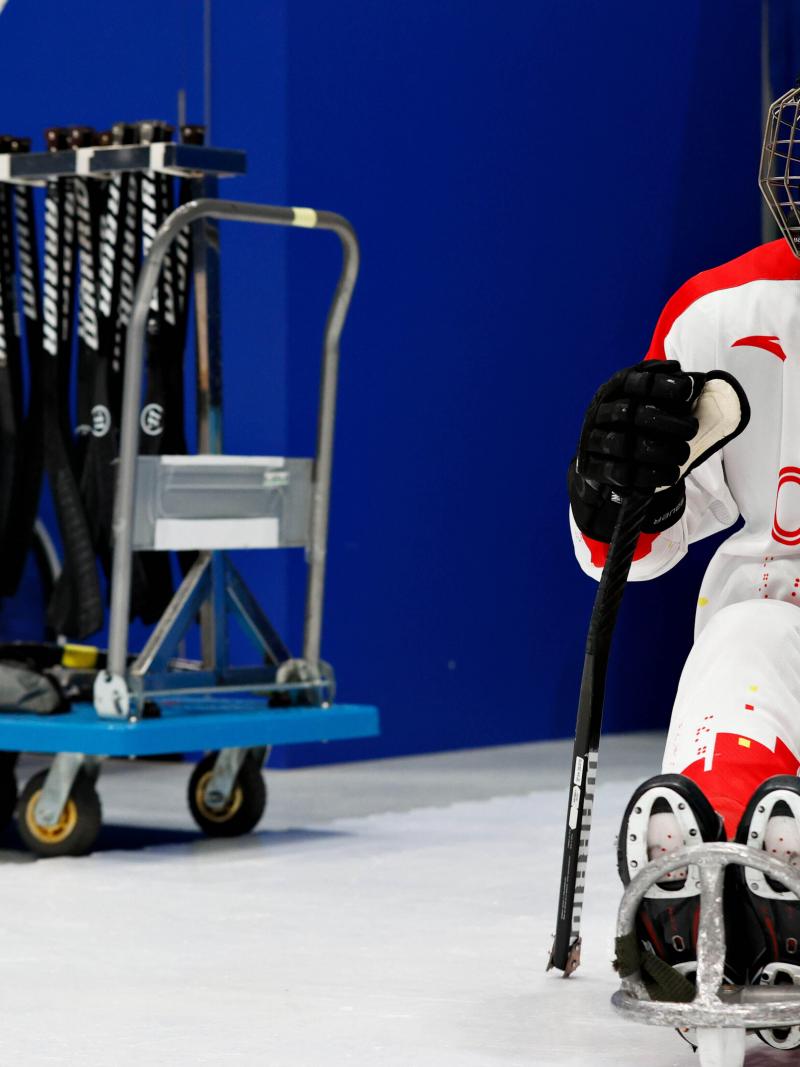 A woman sitting in a sled with a full Para ice hockey gear on her.