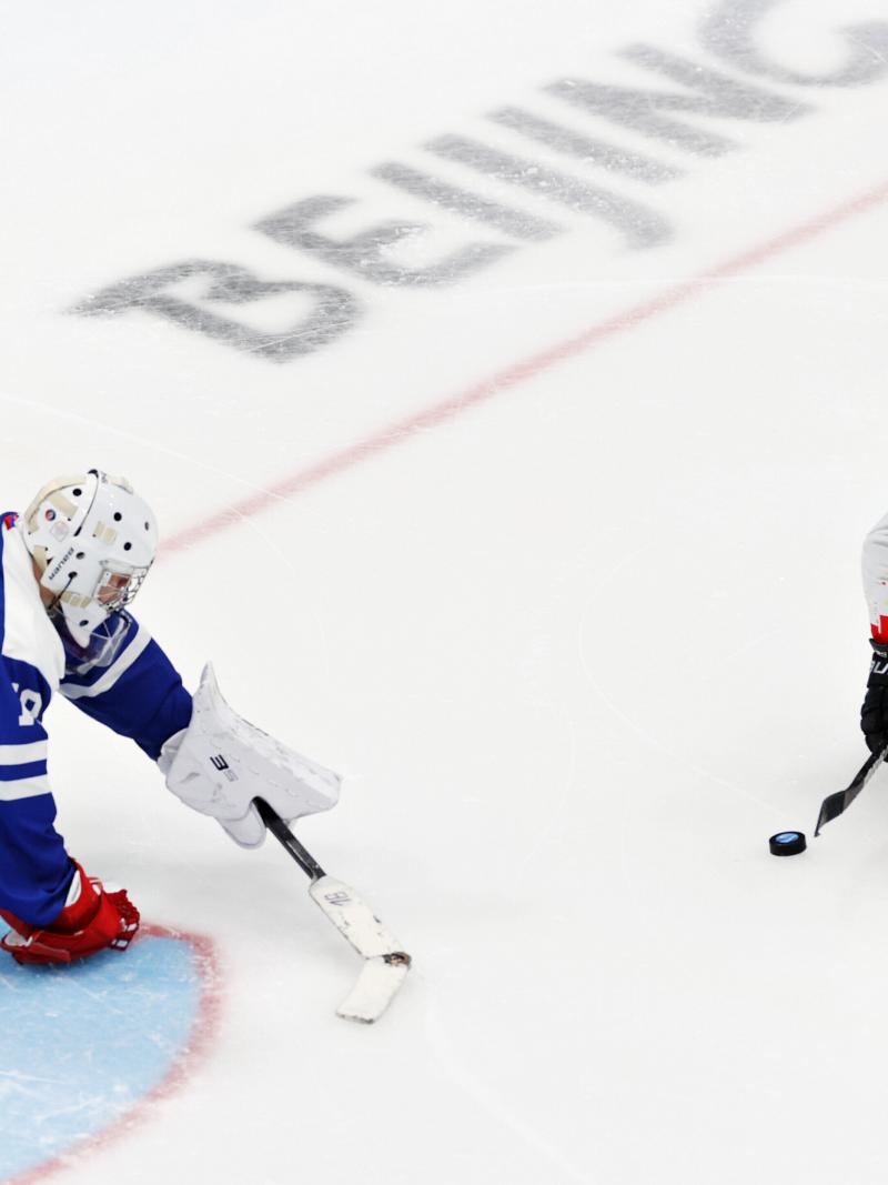 A Para ice hockey player moves past the goalie navigating the puck with a stick.