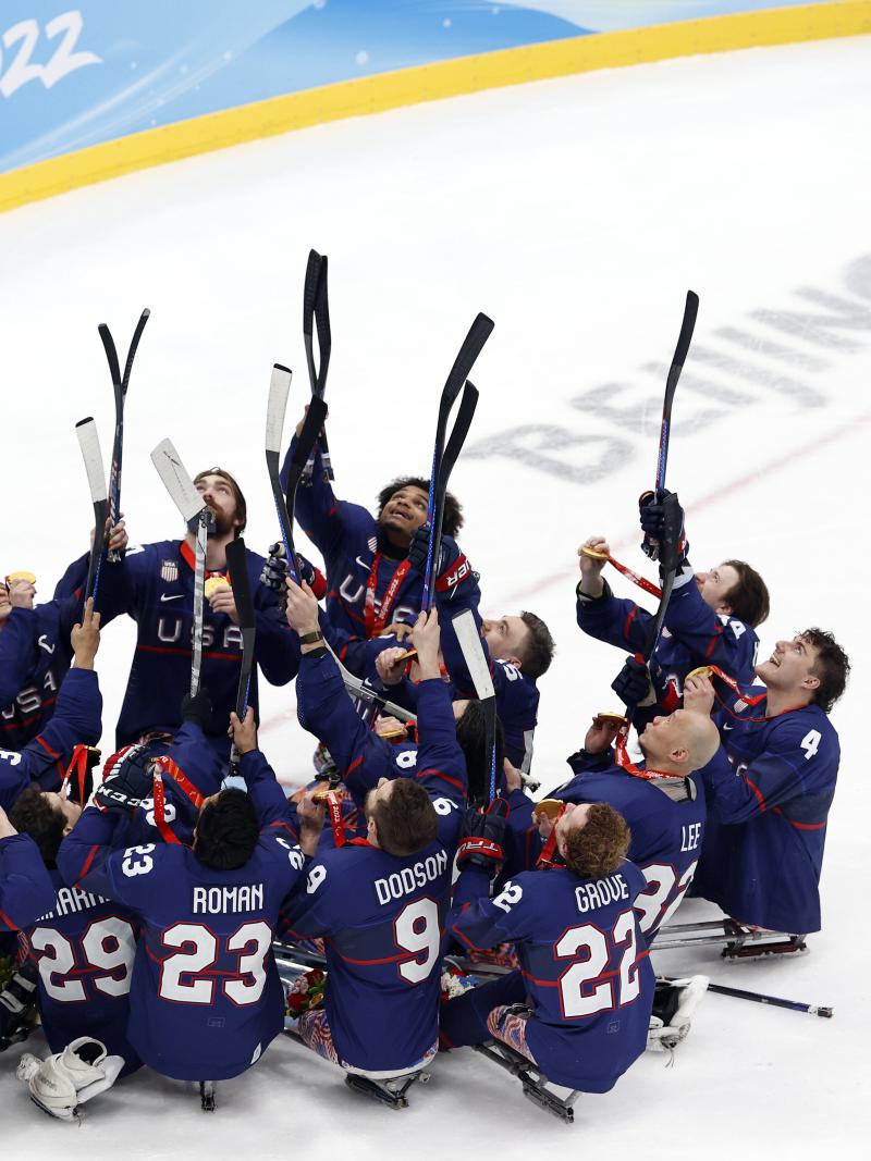 Team USA Para Ice Hockey players in full gear without helmets pointing with their sticks towards the top of the arena.