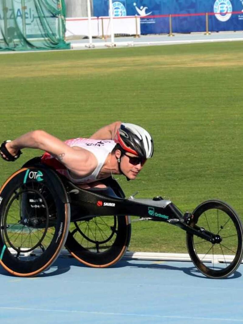 An athlete in a racing wheelchair pushing himself forward with both hands.