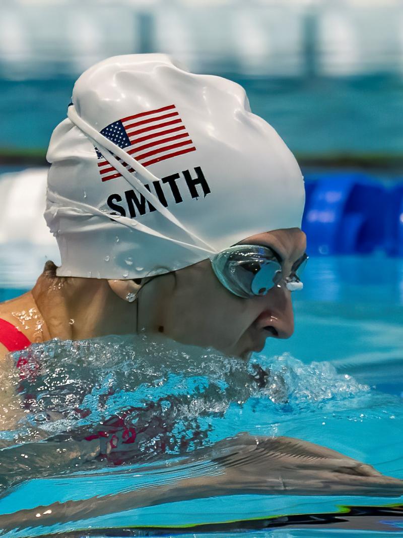 A female Para swimmer with a white cap swimming breastroke