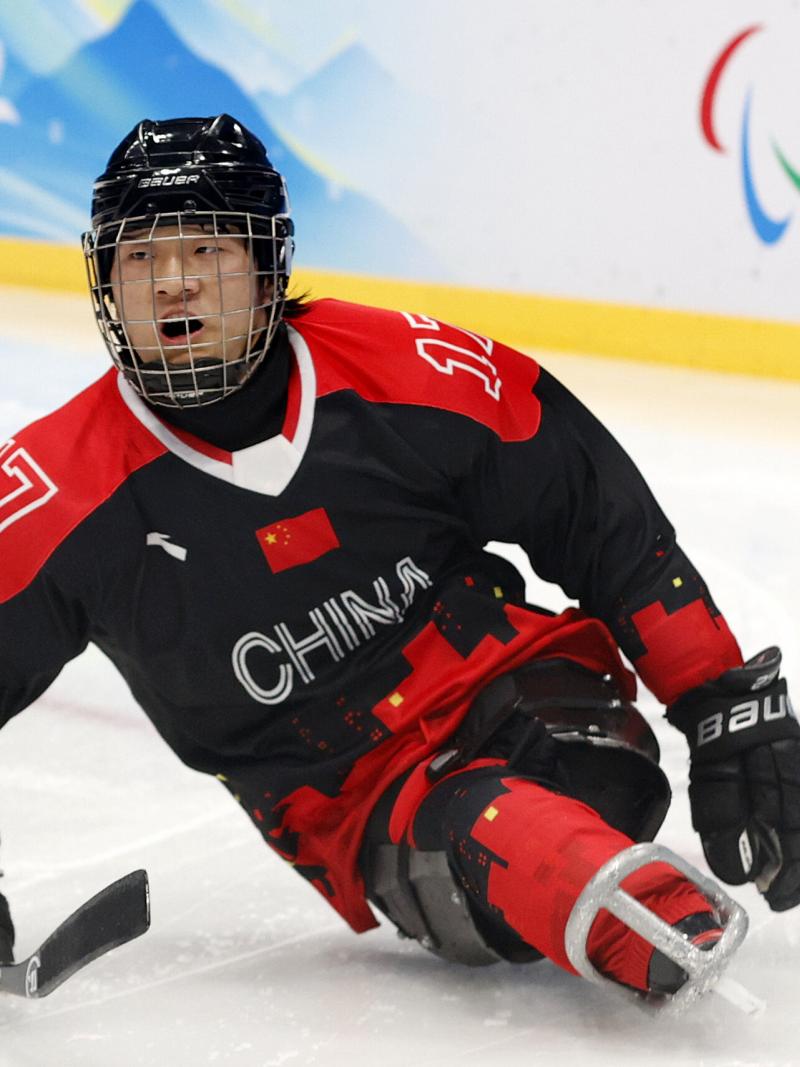 A Para ice hockey player in full gear slides on the ice.