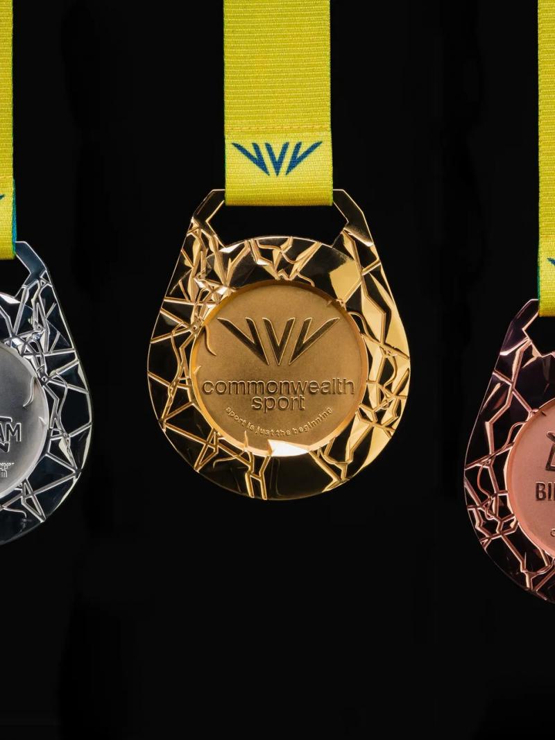 Three medals, gold, silver and bronze, are featured on a black background, each medal having a unique embossed design that symbolises an aerial map of the host region's road and canal network. 