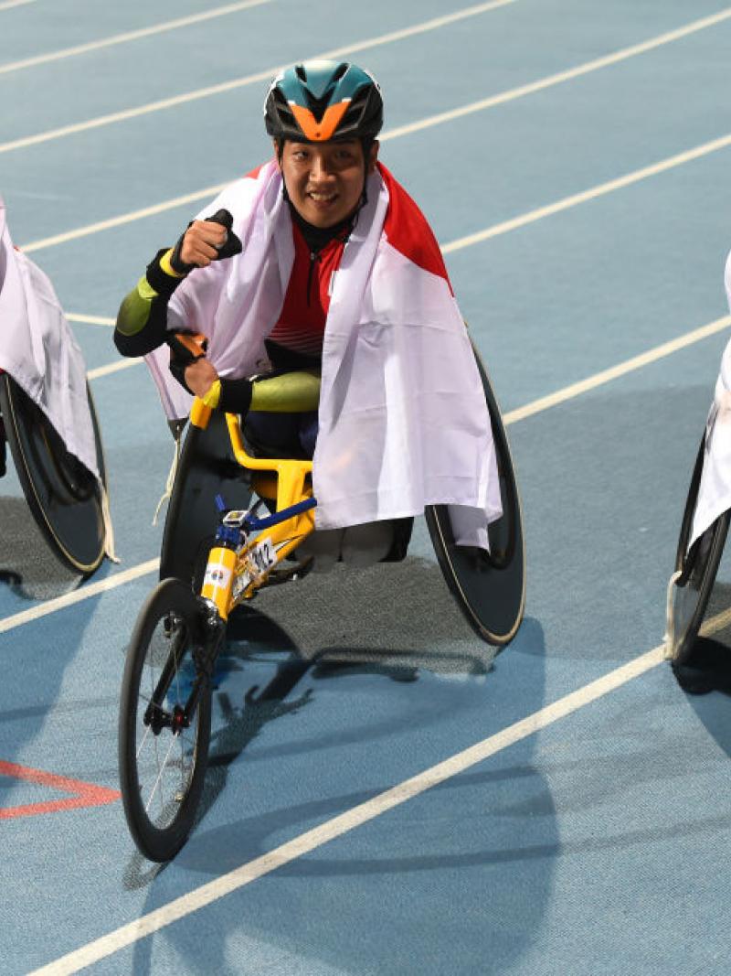 Three men in racing wheelchairs on an athletics track
