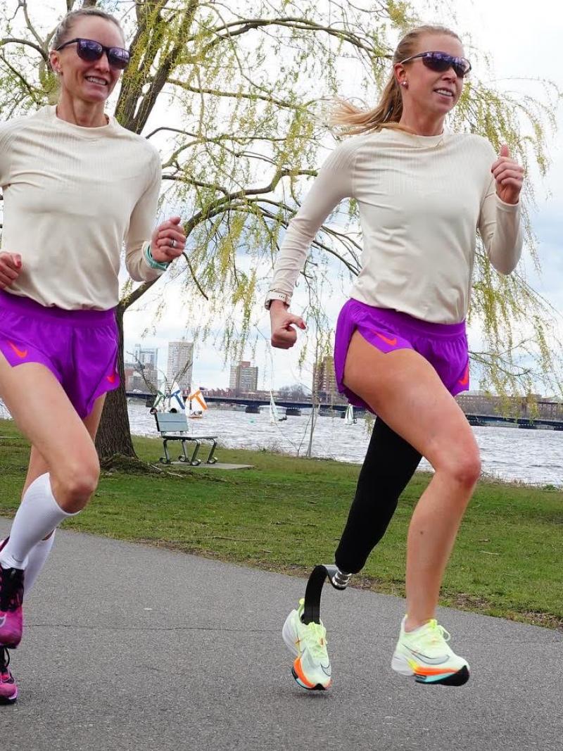 Adrianne Haslet and Shalane Flanagan wear matching beige and purple outfits as they run along the bay during training for the 2022 Boston Marathon.