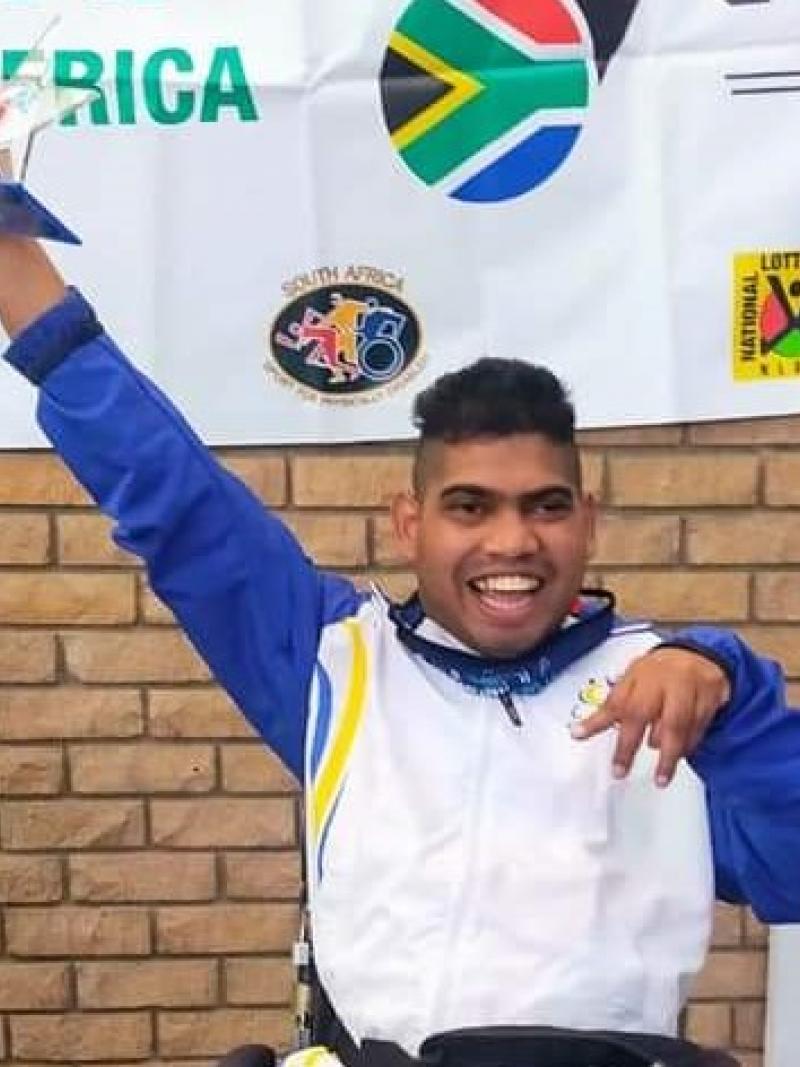 Liakath Aziz raises his arm in celebration while holding a trophy.