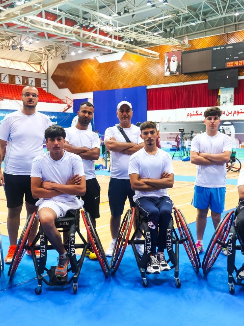 Eight athletes and staff of the Iraqi Para badminton team pose for a photo near the court.