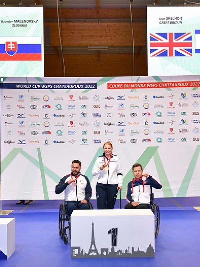 A woman standing on a podium between two men in wheelchairs