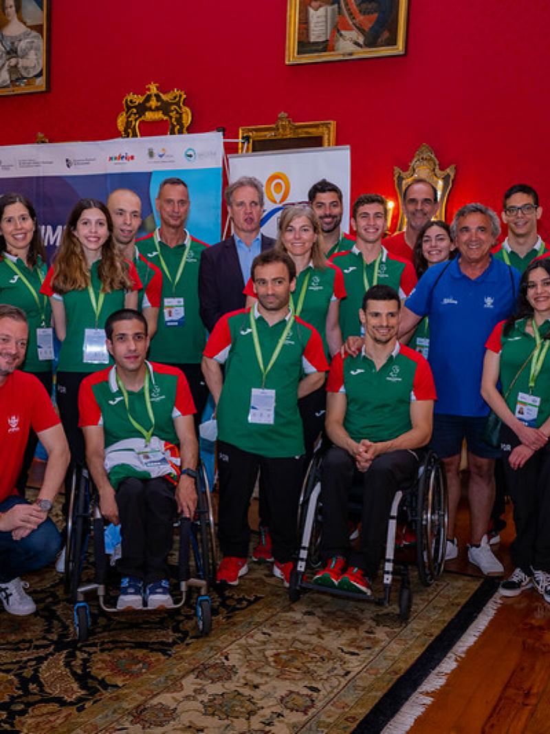 A group of people wearing the uniform of the Portuguese Para swimming team posing for a picture in a hall