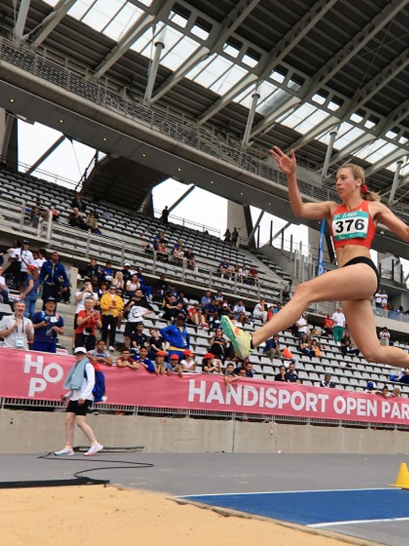 A woman competing in the long jump in front of the spectators in a stadium