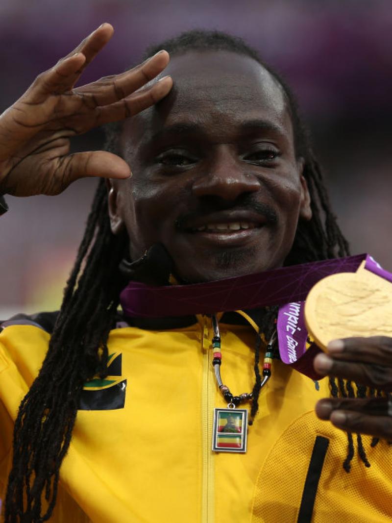 Jamaica's Alphanso Cunningham holds up his gold medal in the men's javelin throw F52/53 and waves with his other hand while posing for photos on the London 2012 podium.
