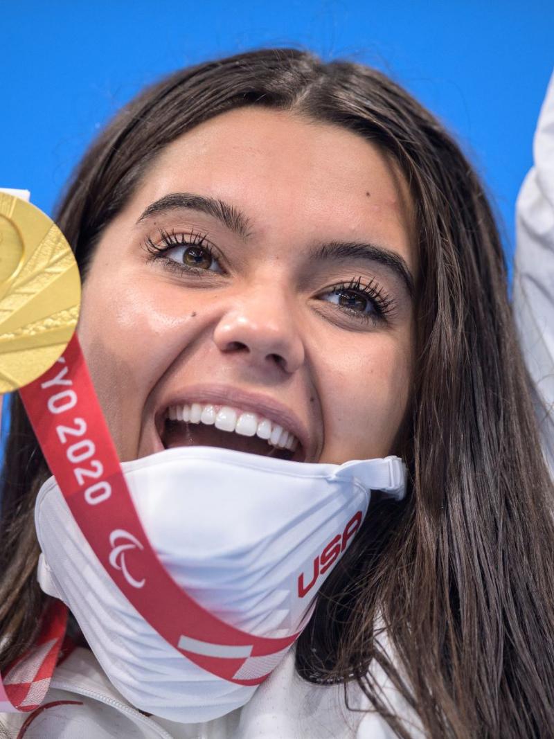 Anastasia Pagonis smiles widely as she holds up her gold medal and raises her other arm in celebration at Tokyo 2020.