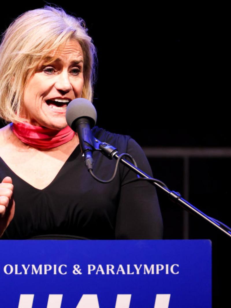 A woman makes a speech at a tribune marked with the words 'U.S. Olympic and Paralympic Hall of Fame'.