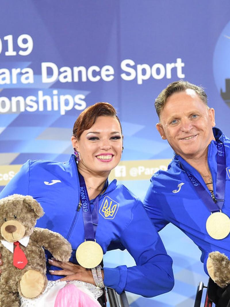 Image of a male and a female dancer in their wheelchairs and with their gold medals
