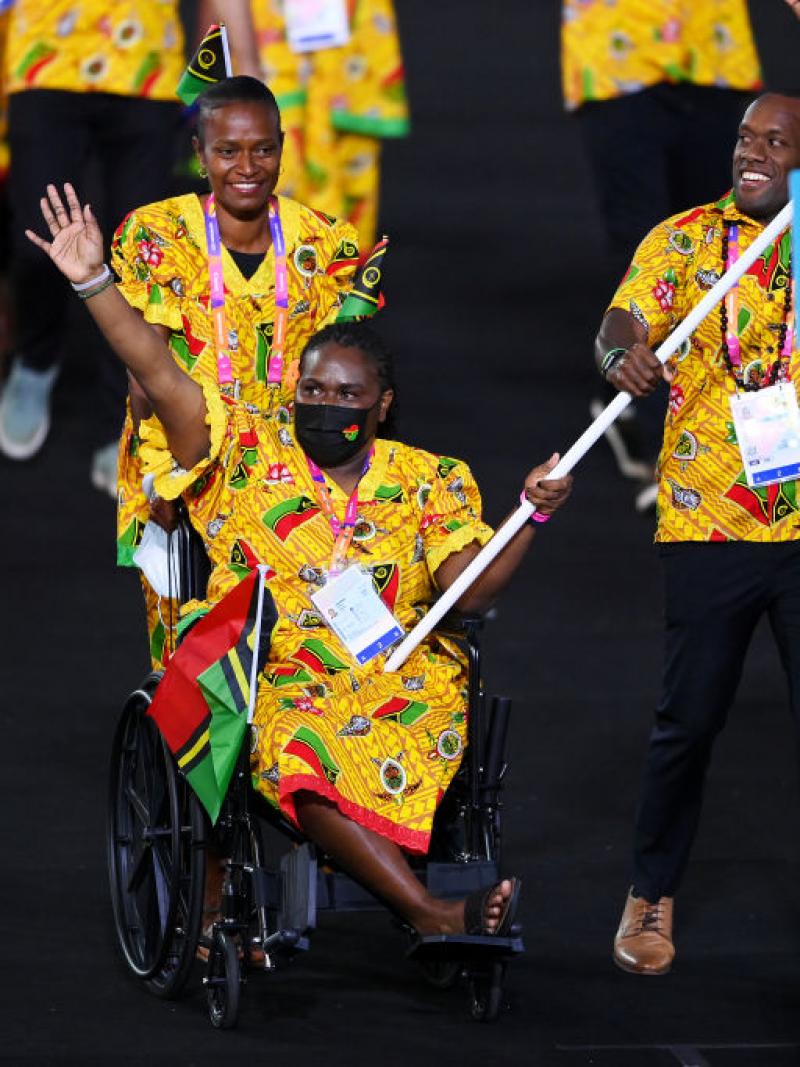 A woman in traditional clothes and in a wheelchair carries the Vanuatu flag in an athlete's parade.