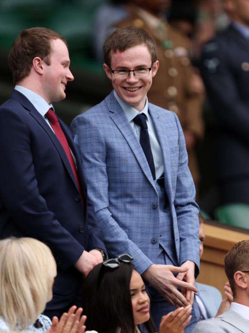 Two young men stand and smile as people around them sit and clap.