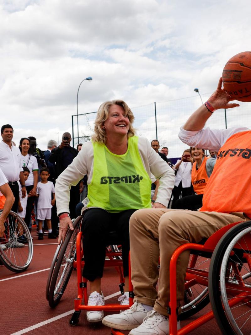 One woman and two men try out wheelchair basketball surrounded by spectators.
