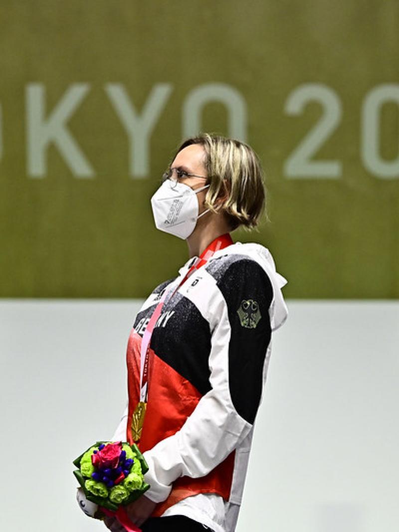 Image of a female Para shooter after winning gold, looking at the German national flag on the podium