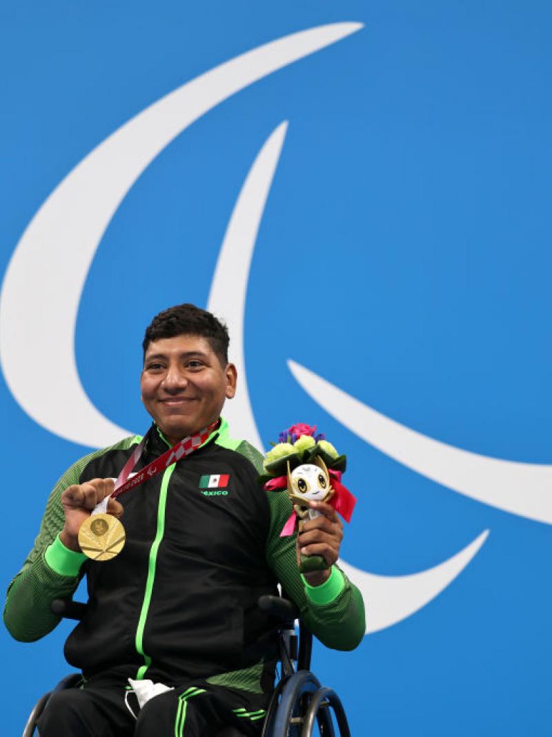 Image of a male Para swimmer in the podium with his gold medal and his flowers
