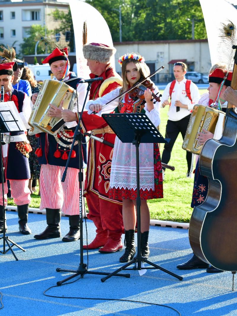 A group of musicians in traditional Polish clothing play on the athletics track in Cracow.